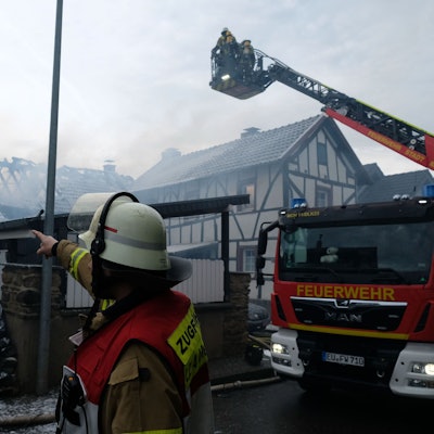 Zwei Einsatzkräfte sowie ein Drehleiter-Fahrzug der Feuerwehr stehen vor dem gelöschten Gebäude.