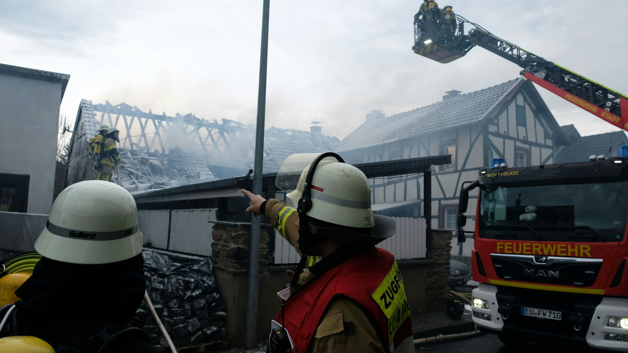 Zwei Einsatzkräfte sowie ein Drehleiter-Fahrzug der Feuerwehr stehen vor dem gelöschten Gebäude.