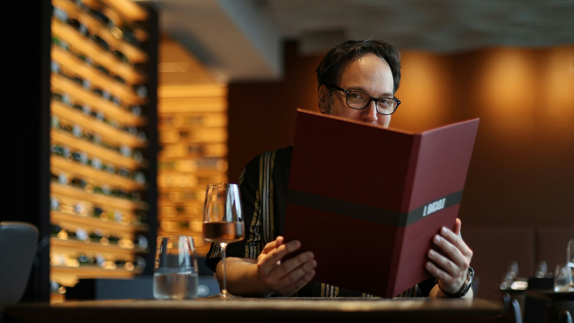 Carsten Henn hält eine geöffnete Speisekarte halb vor das Gesicht