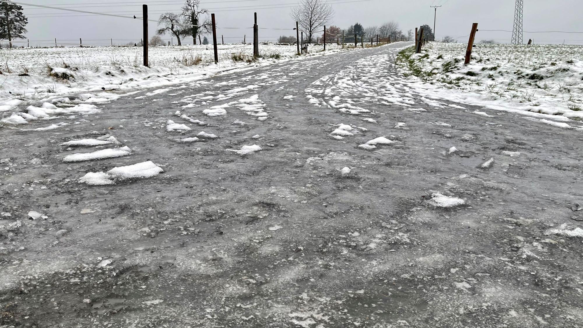 Eine dicke Eisschicht liegt auf der Straße. Felder sind mit Zäunen abgetrennt.