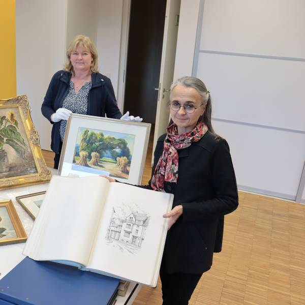 Zeichnungen und Gemälde des Euskirchener Malers Willy Loos, die Enkelin Iris Pütz an Leiterin Heike Lützenkirchen und deren Mitarbeiterin Jennifer Kirchhoff überreicht, sind auf einem Tisch ausgebreitet.