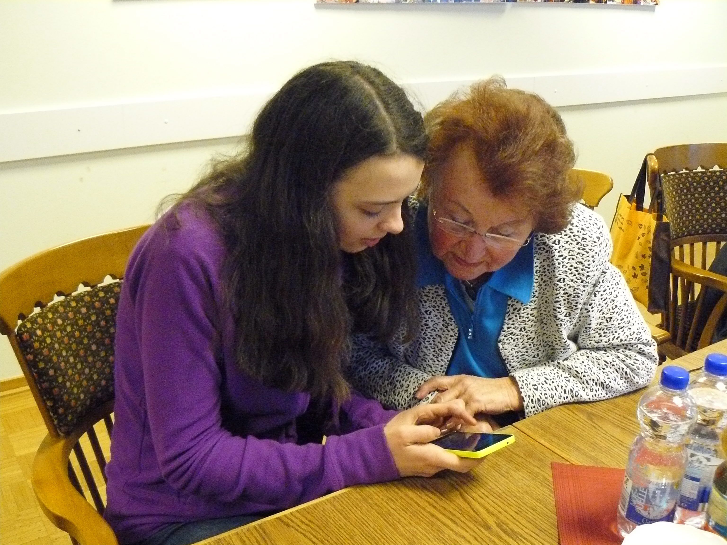 Eine Jugendliche bringt einer Seniorin die Bedienung ihres Smartphones bei.