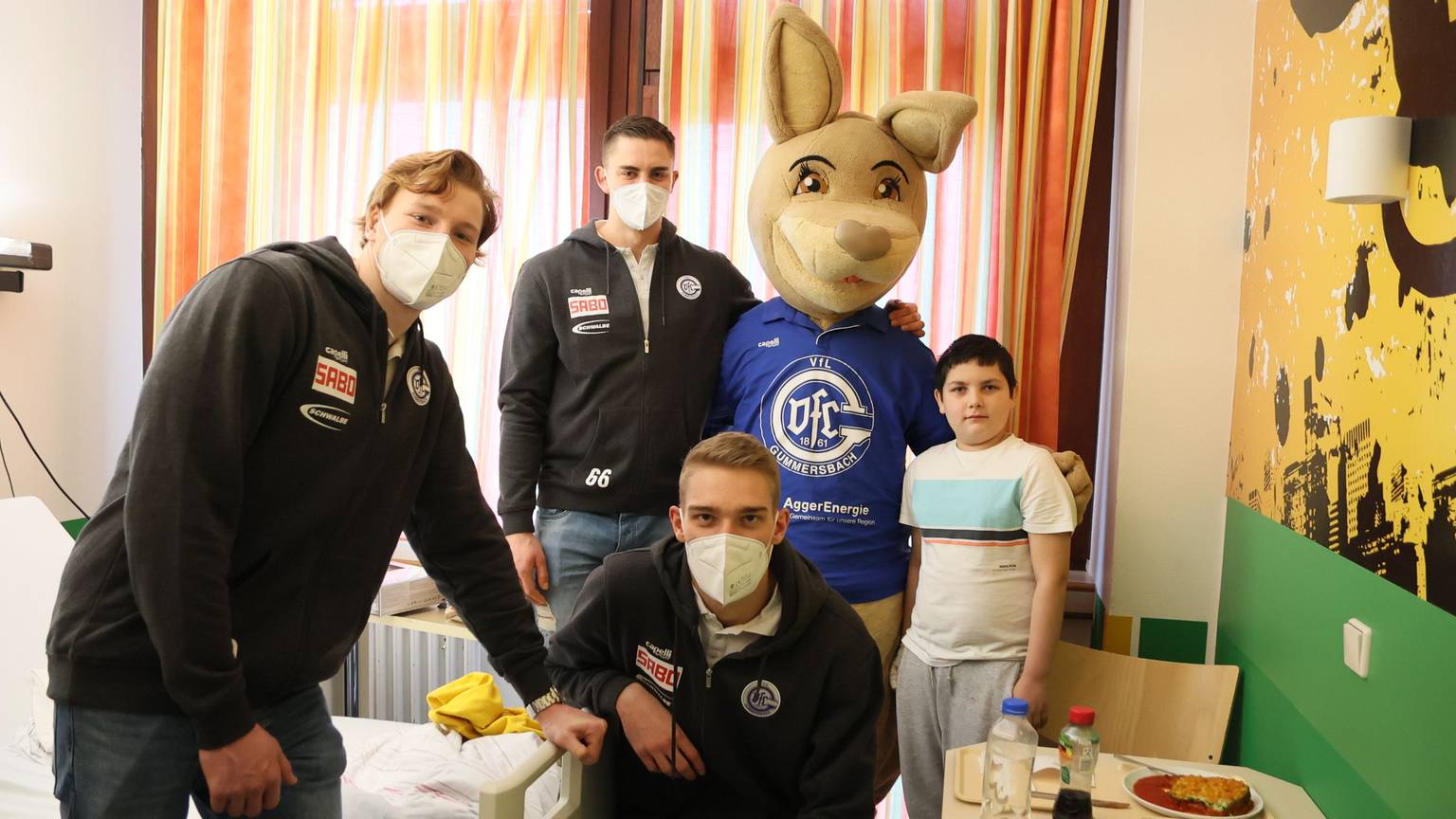 Die Handballspieler Tom Kiesler, Stepan Zeman und Tom Jansen posieren mit dem lebensgroßen VfL-Maskottchen, dem Känguru Gummi und dem zehn Jahre alten Ben für ein Gruppenfoto in einem Krankenzimmer der Kinderklinik.