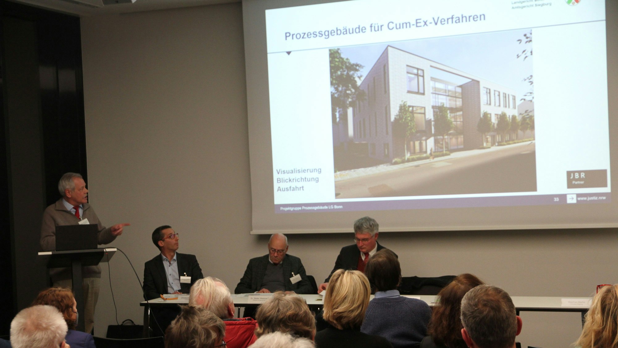 Bürgerinnen und Bürger sitzen vor einem Experten-Panel, an die Wand werden Visualisierungen der Anbau-Pläne projiziert.