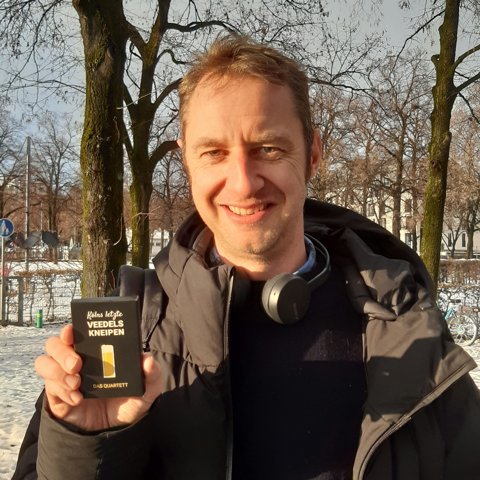 Ein Mann in Winterjacke hält ein Kartenspiel hoch.