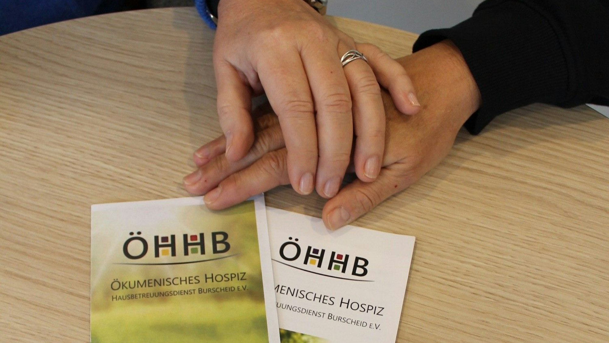 Hospizverein Burscheid: zwei Hände berühren einander neben den Faltblättern des Vereins