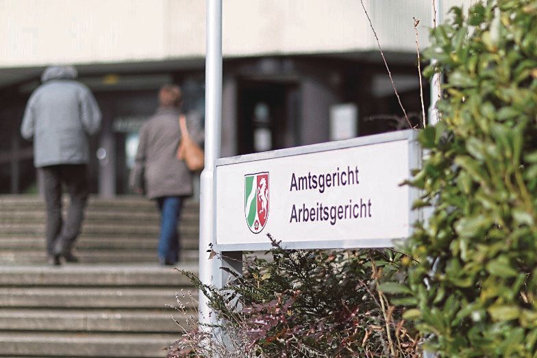 Das Schild des Amtsgerichts im Vordergrund und zwei Menschen im Hintergrund, die das Gericht betreten.