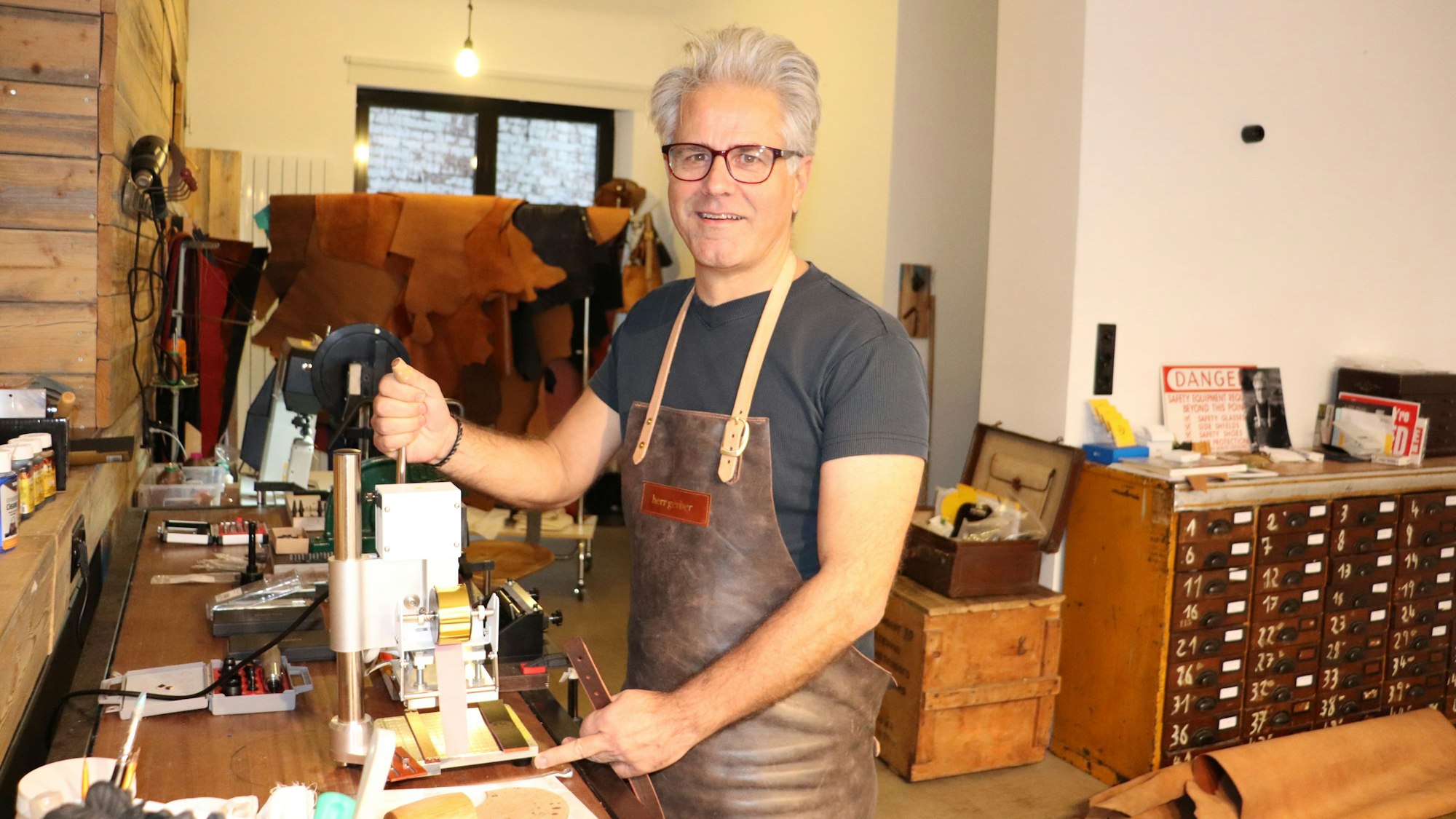 Jürgen Gerber steht an einer Maschine an seinem Arbeitstisch, im Hintergrund sieht man das Geschäft.