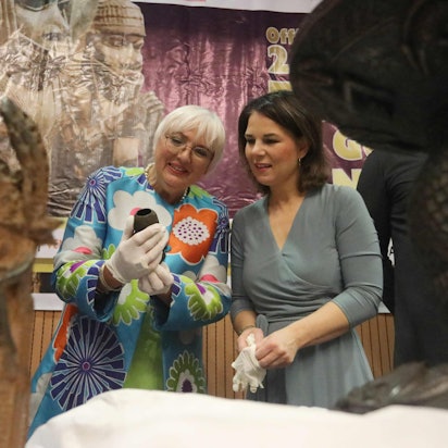 Claudia Roth (m) und Annalena Baerbock im nigerianischen Außenministerium in Abuja bei der Übergabe des Artefakts aus Benin-Bronze. Roth hält es und beide gucken es an.