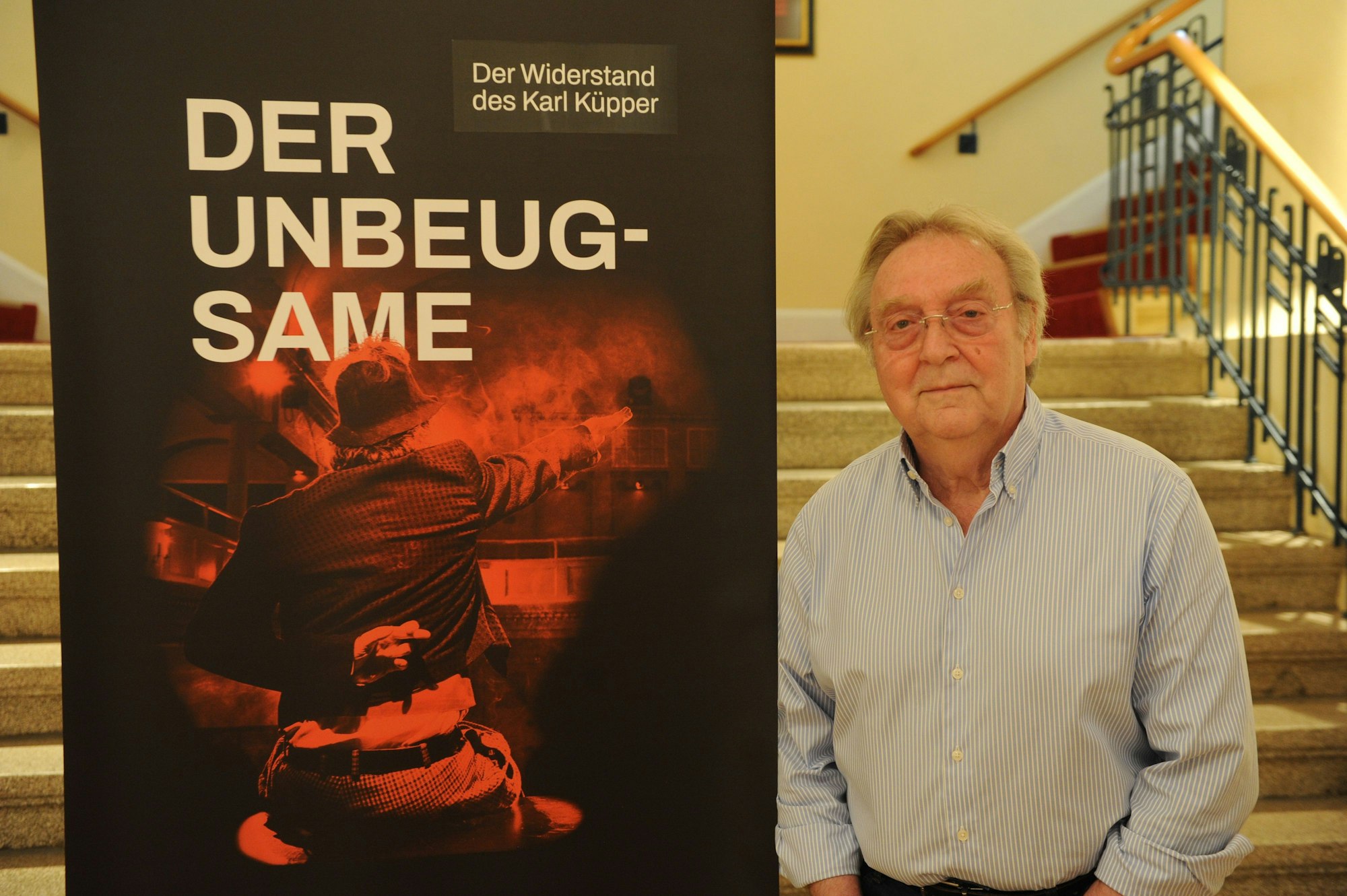 Ein Aufsteller von „Der Unbeugsame“, daneben steht ein Mann.