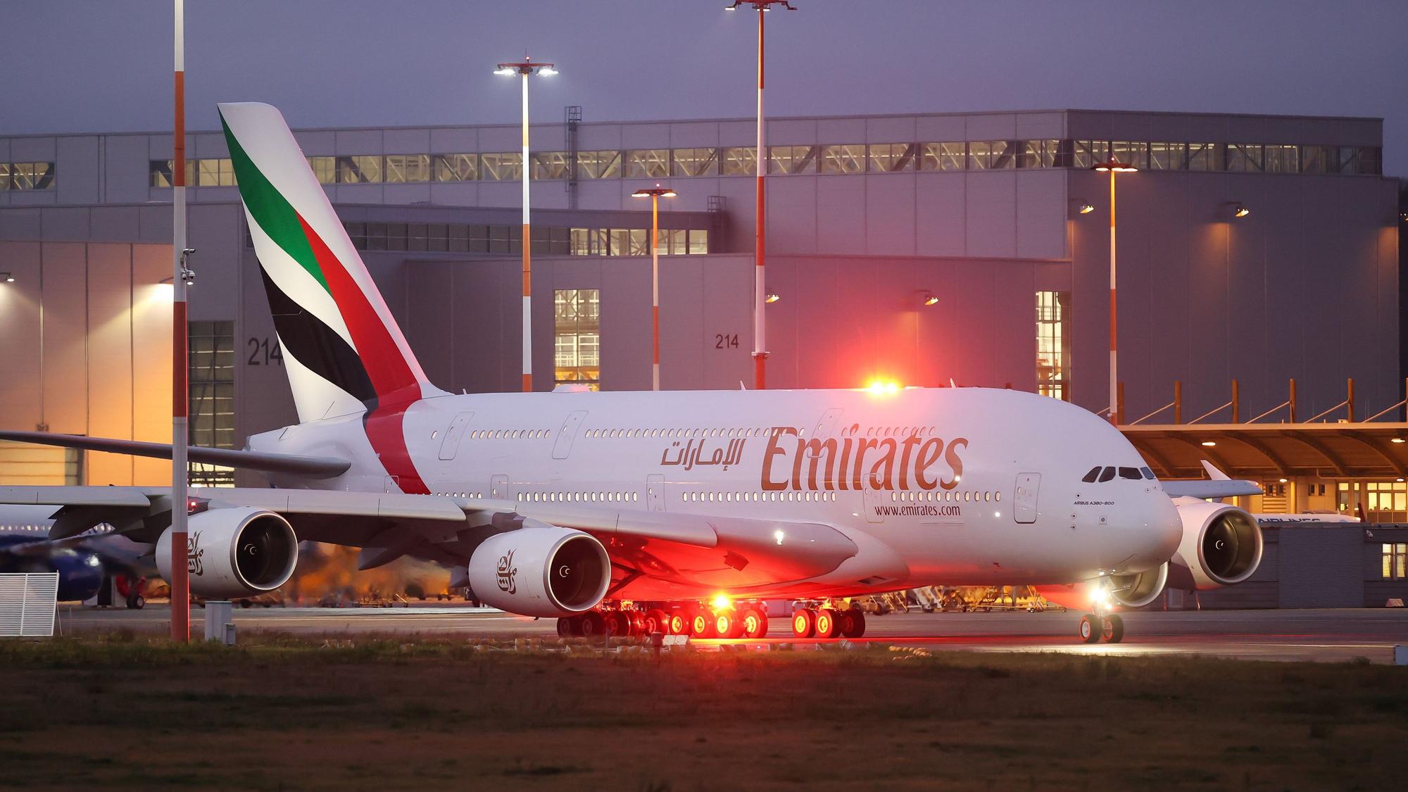 Ein Airbus A380 der arabischen Fluggesellschaft Emirates rollt zur Start- und Landebahn. Er wird von mehreren Lichtern beleuchtet.