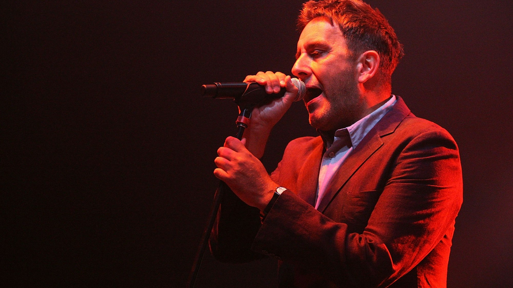 Terry Hall bei einem Auftritt. Er hält ein Mikrofon in der Hand.