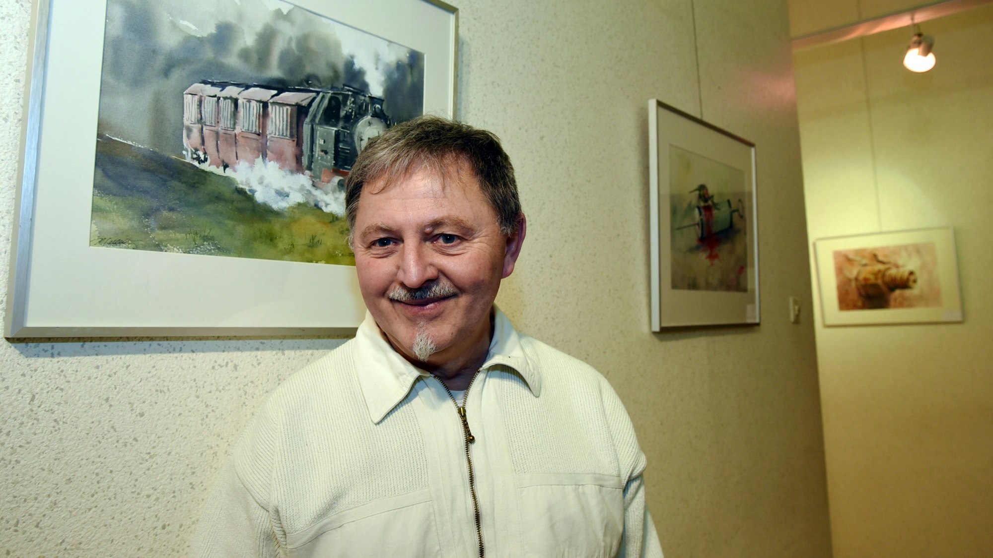 Henry Schellenberg steht vor einer Wand, an der mehrere Zeichnungen hängen.