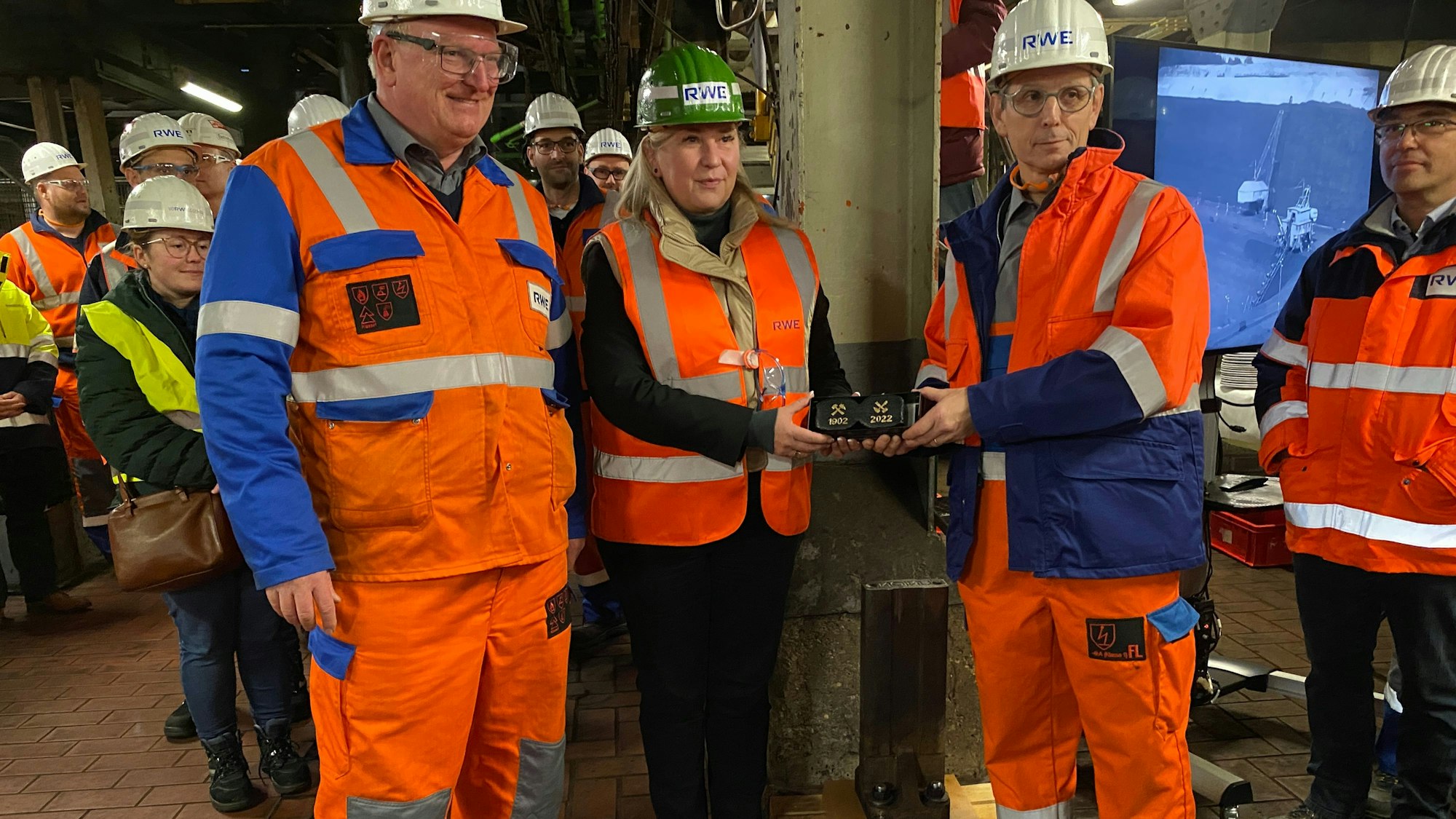 Susanne Stupp bekommt Briketts überreicht, um sie herum stehen Männer in Warnwesten und Sicherheitshelmen.