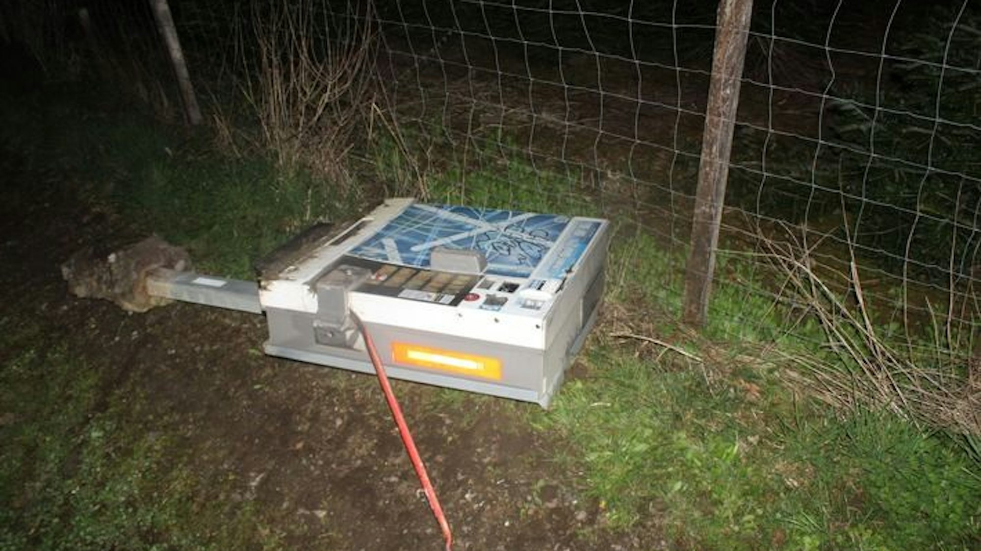 Ein Zigarettenautomat liegt aus der Verankerung gerissen auf einem Wirtschaftsweg.