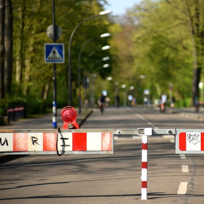 Im Hitergrund sieht man eine gesperrte Straße mit zwei Streifen. Links und rechts wachsen Bäume.
