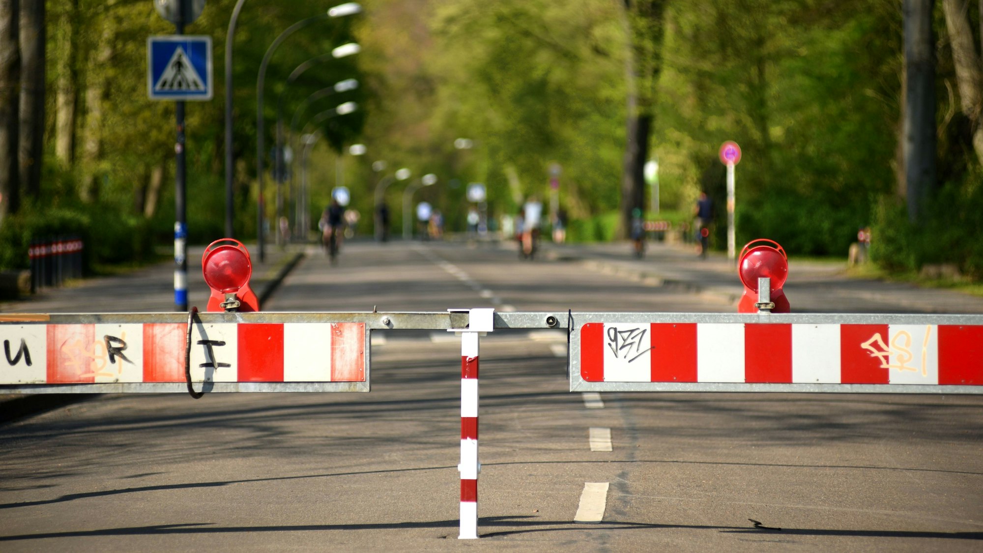 Im Hitergrund sieht man eine gesperrte Straße mit zwei Streifen. Links und rechts wachsen Bäume.
