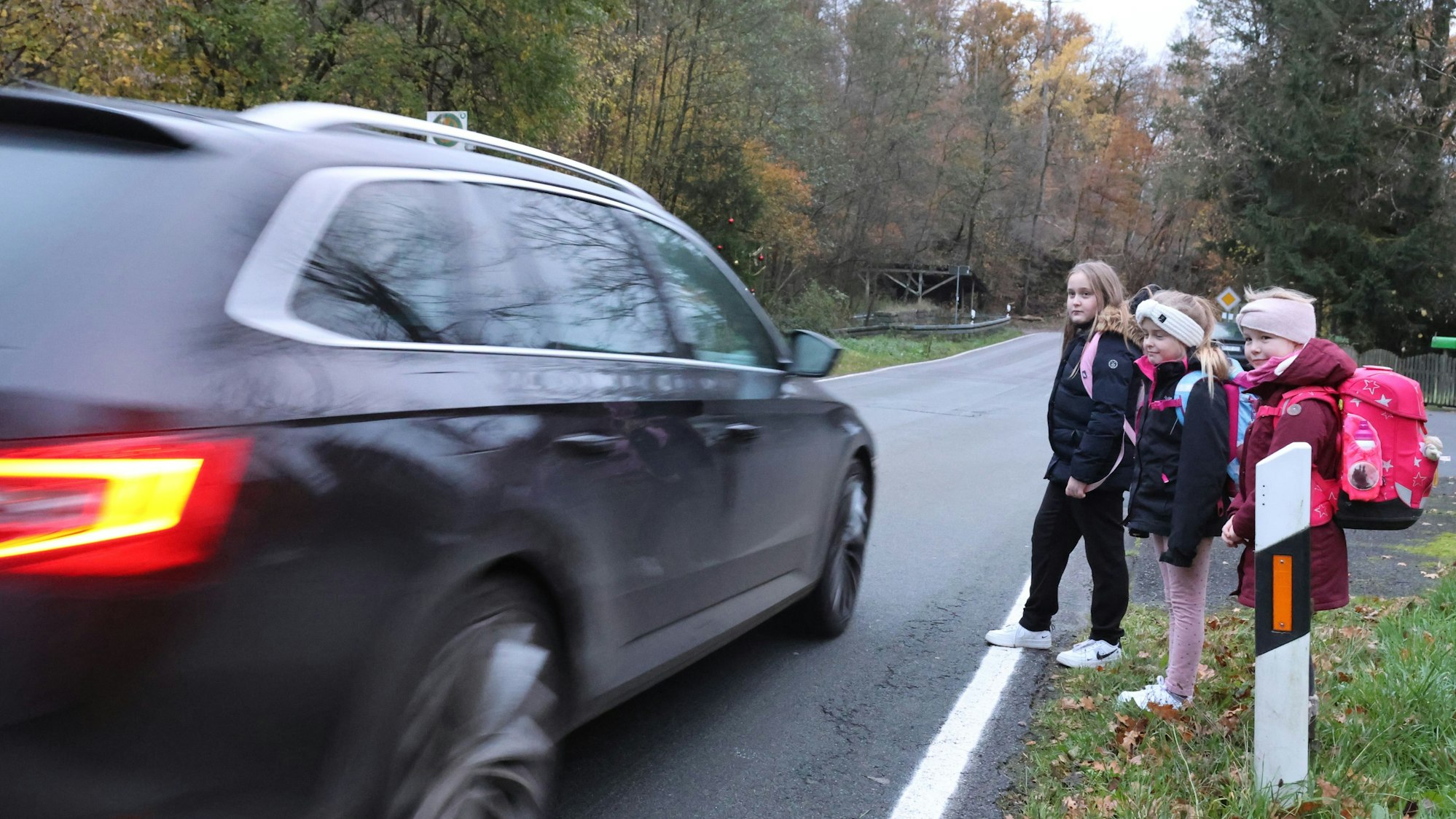 Drei Schulkinder stehen am Rand der L 320. Diese viel befahrene Straße müssen sie auf dem Weg zum Schulbus überqueren.