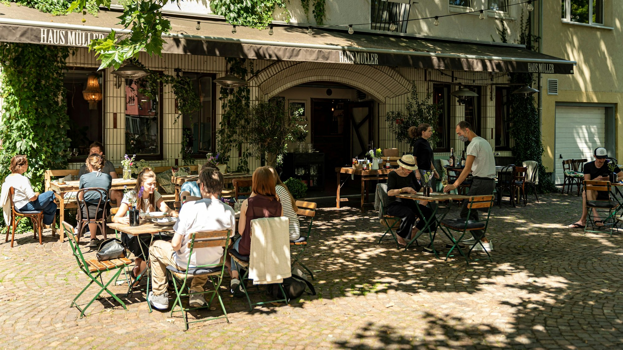 Das Haus Müller von außen mit Plätzen in der Sonne und im Schatten unter dem Baum.