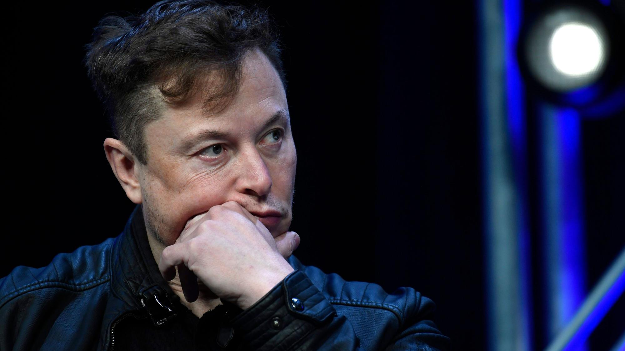 Tech-Milliardär Elon Musk sitzt mit einer Lederjacke auf einem Stuhl, er stützt den Kopf auf seinen Arm.