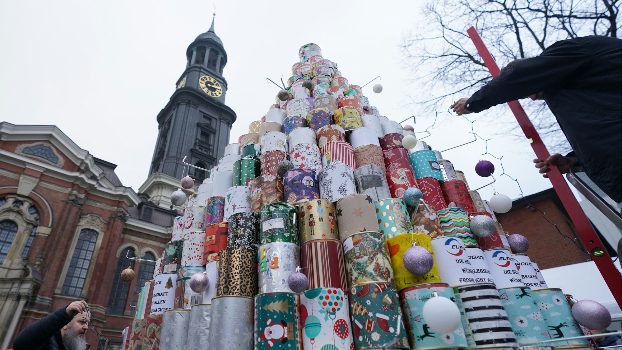 Schülerinnen und Schüler und Helfer schmücken den größten Weihnachtsbaum aus Konservendosen auf dem Kirchplatz vor der Hamburger Hauptkirche Sankt Michaelis.