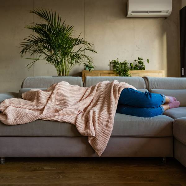 Eine junge Frau liegt auf einem Sofa und ist von einer Decke bedeckt.