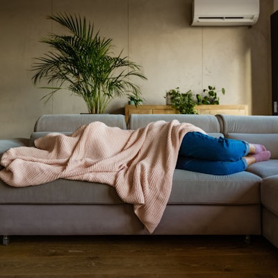 Eine junge Frau liegt auf einem Sofa und ist von einer Decke bedeckt.