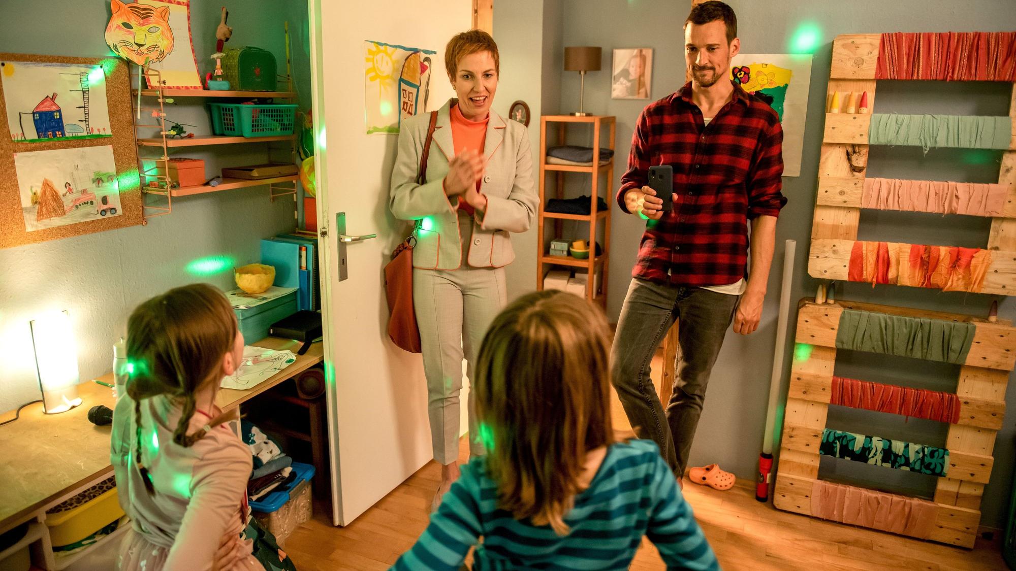 Nora Boeckler als Frau Steck vom Jugendamt im Kinofilm Oskars Kleid, rechts neben ihr steht Florian David Fitz, im Vordergrund sind zwei Kinder zu sehen.