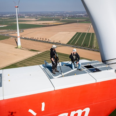 Personen stehen auf einem Windrad. In NRW soll die Abstandsregel für Windräder zu Siedlungen fallen. (Symbolbild)