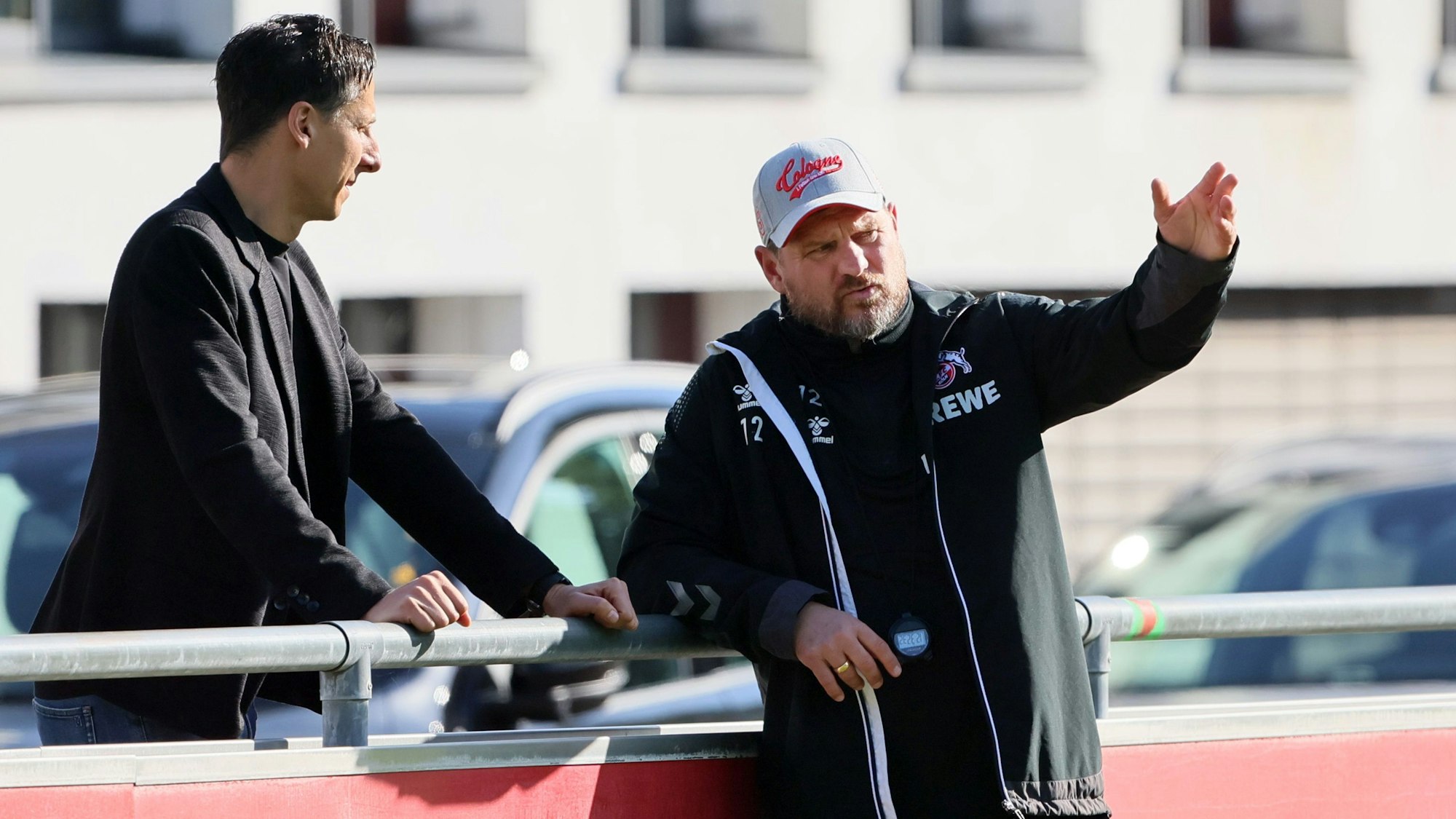 FC-Geschäftsführer Christian Keller und Trainer Steffen Baumgart unterhalten sich am Rande des Trainings des 1. FC Köln am Geißbockheim. Baumgart lehnt an der Bande und gestikuliert, Keller steht dahinter.