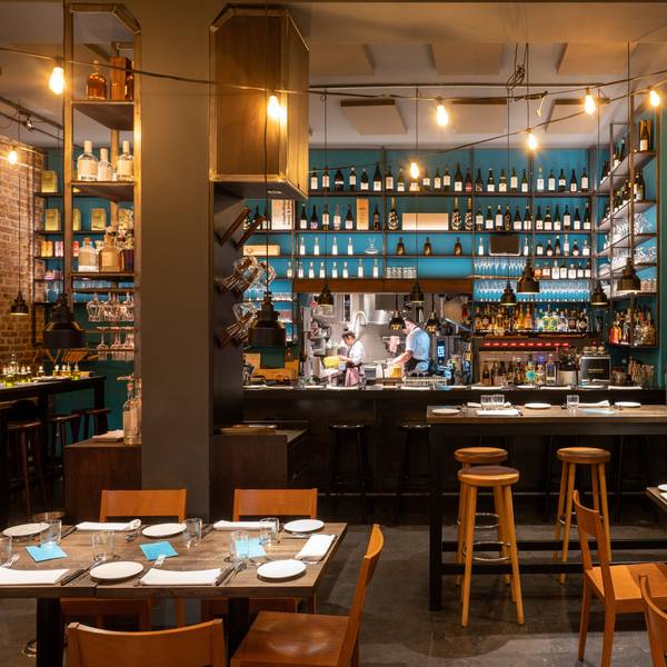 Innenraum eines Restaurants mit Holzstühlen und -tischen, im Hintergrund eine Bar