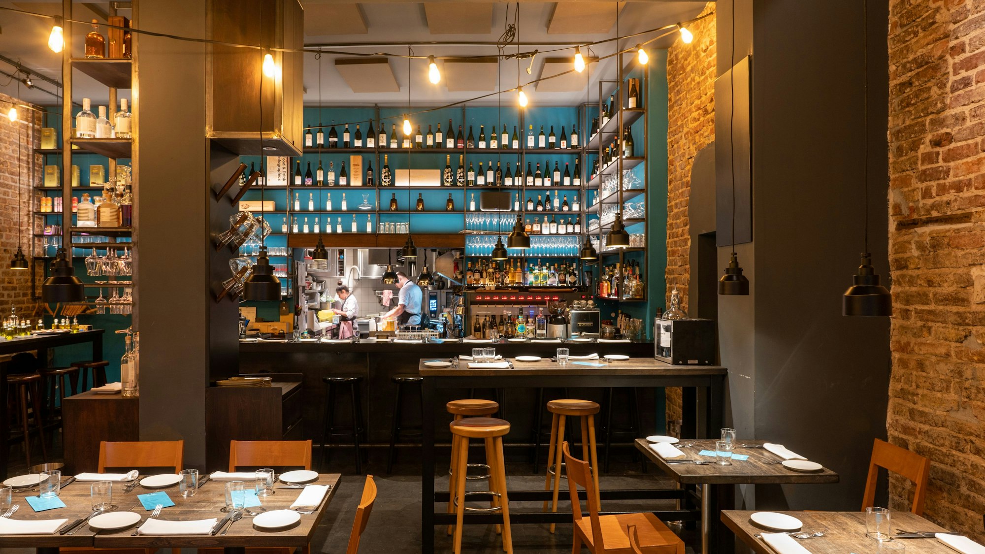 Innenraum eines Restaurants mit Holzstühlen und -tischen, im Hintergrund eine Bar