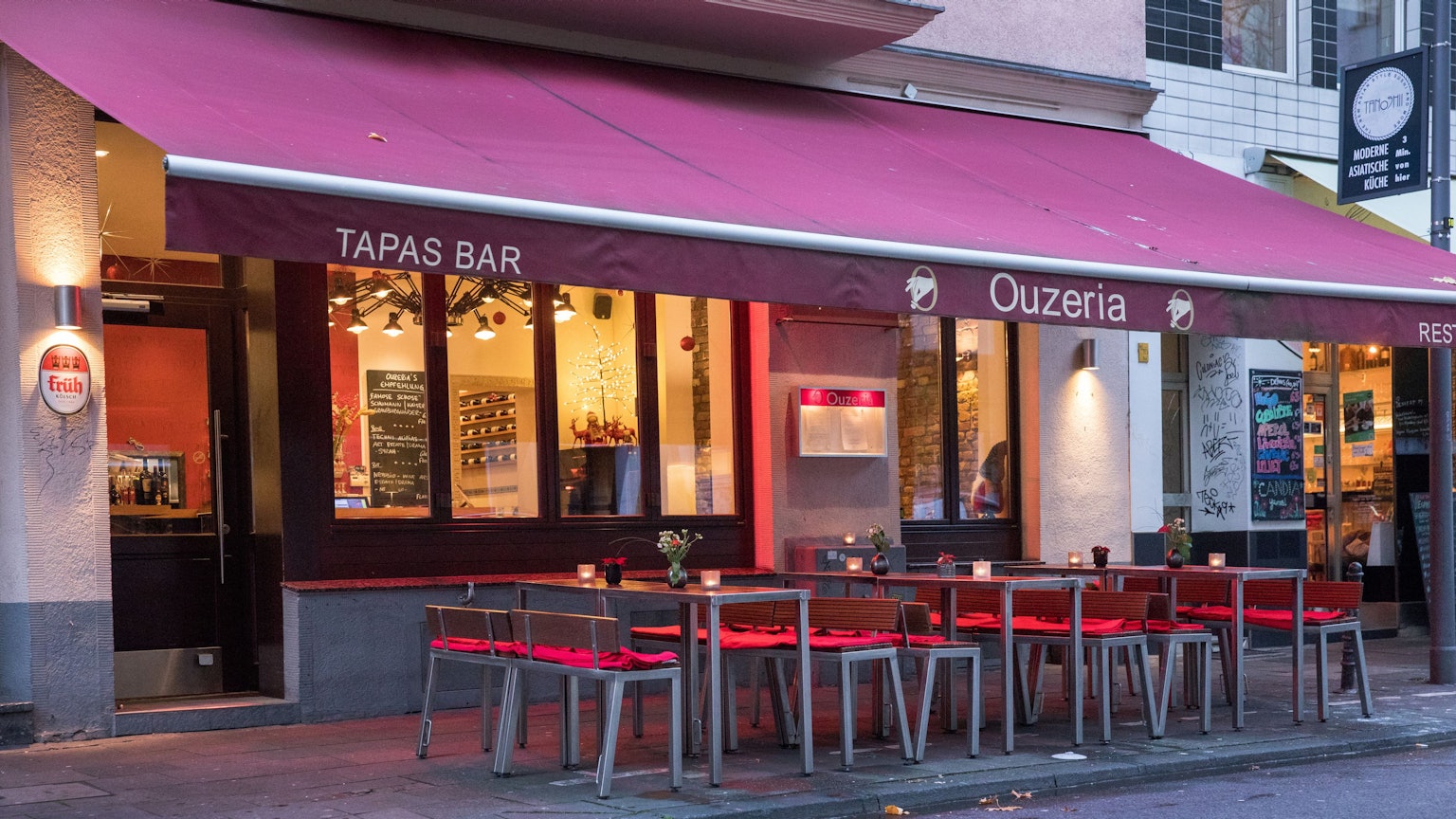 Restaurant von außen mit roter Markise über Tischen und Stühlen