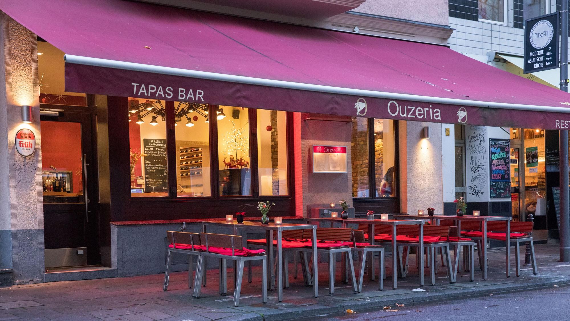 Restaurant von außen mit roter Markise über Tischen und Stühlen