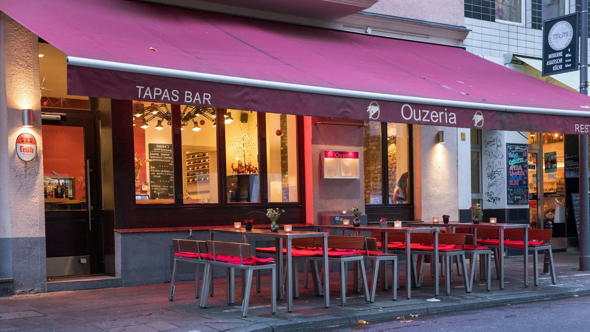 Restaurant von außen mit roter Markise über Tischen und Stühlen