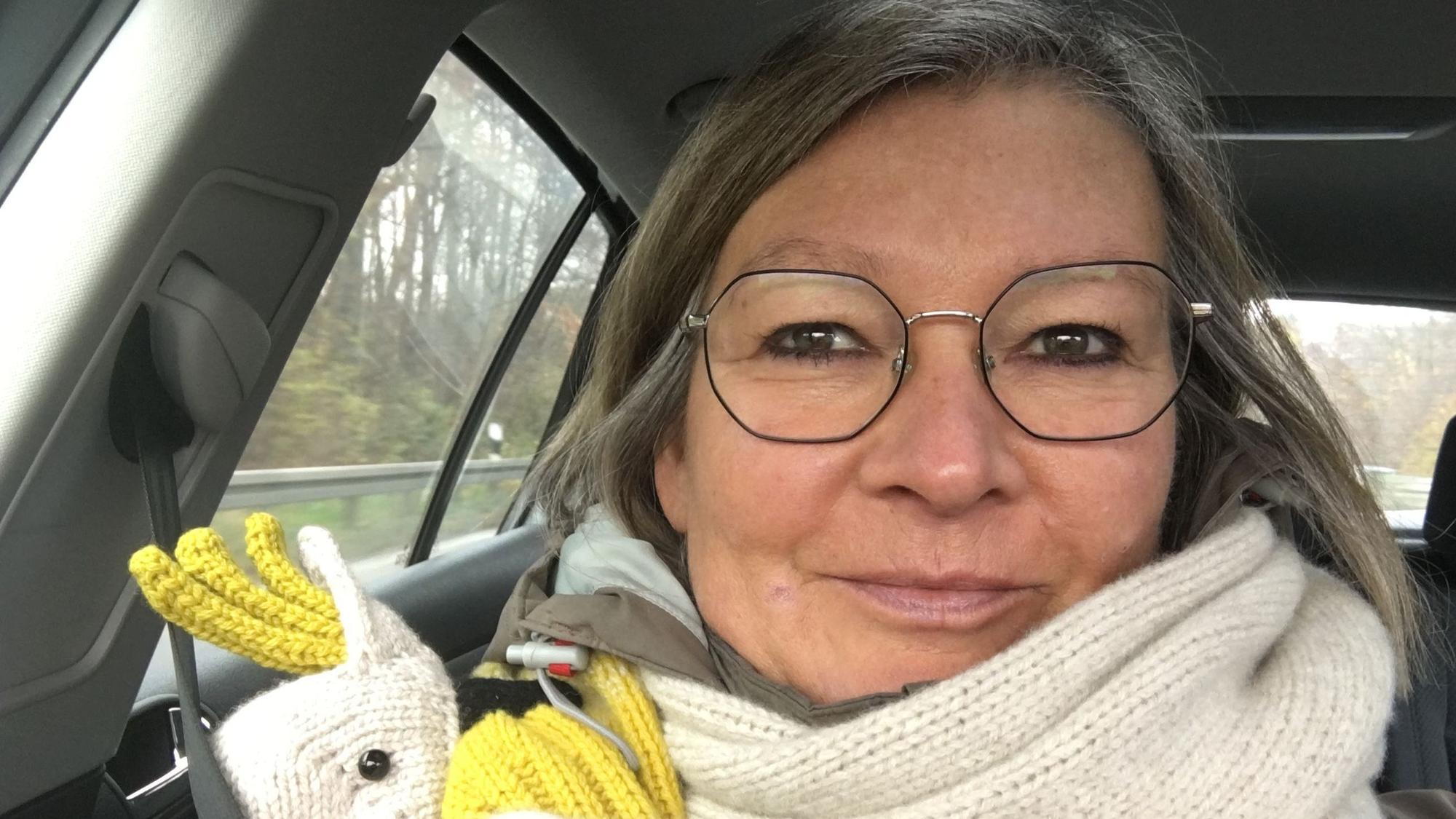 Eine Frau mit weißem Schal und Brille sitzt in einem Auto.