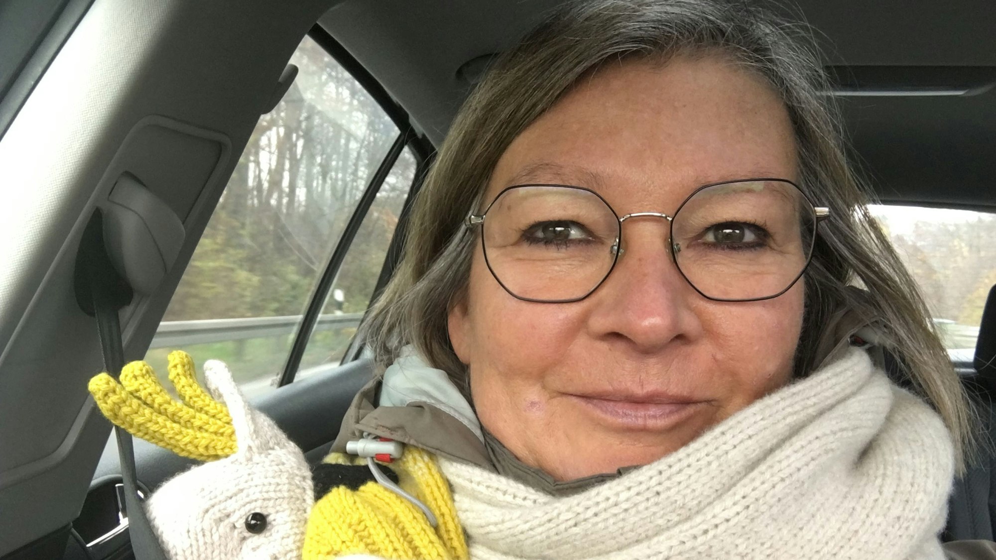 Eine Frau mit weißem Schal und Brille sitzt in einem Auto.