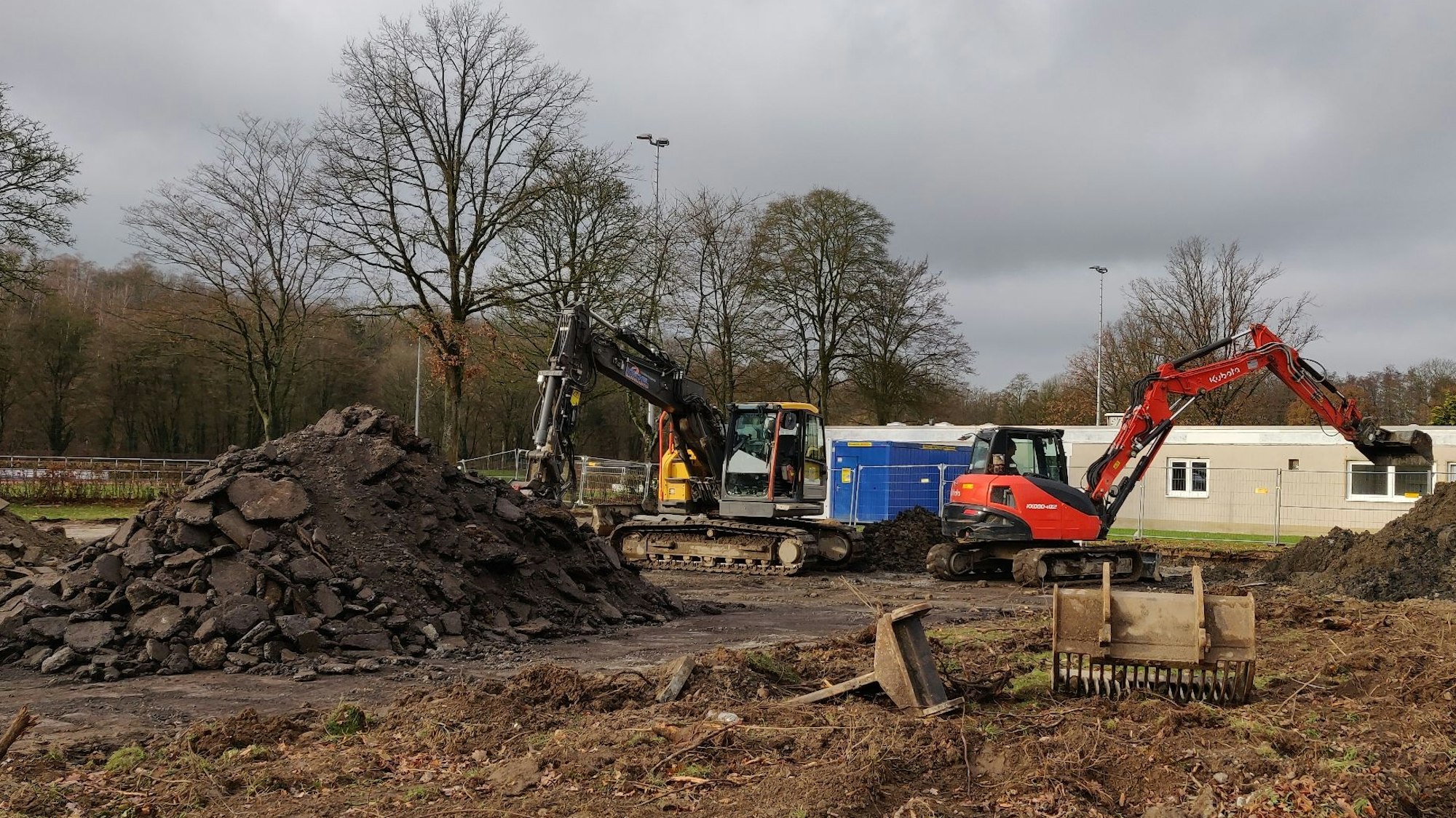 Bagger auf dem Bauplatz. Im Hintergrund der frühere Umkleiden-Trakt, momentan Unterkunft für Geflüchtete aus der Ukraine.