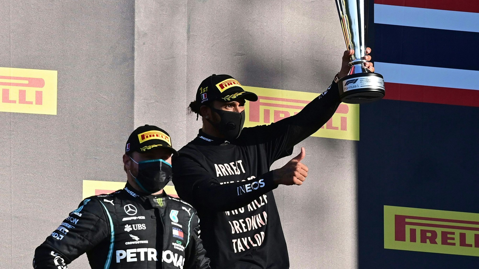 Formel-1-Weltmeisterschaft, Grand Prix der Toskana, Rennen, Autodromo Internazionale del Mugello: Sieger Lewis Hamilton (r) aus Großbritannien vom Team Mercedes freut sich auf dem Podium neben dem Zweitplatzierten Valtteri Bottas aus Finnland vom Team Mercedes und hält die Trophäe nach oben. Hamilton trägt ein Shirt mit der Aufschrift „Arrest the Cops who killed Bronna Taylor“