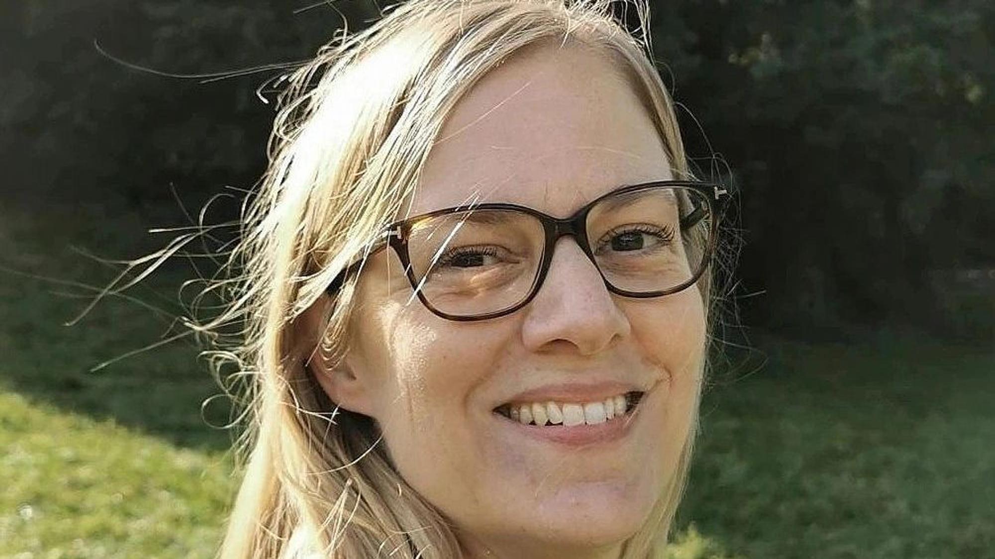 Eine blonde Frau mit blauer Bluse und schwarzer Brille.