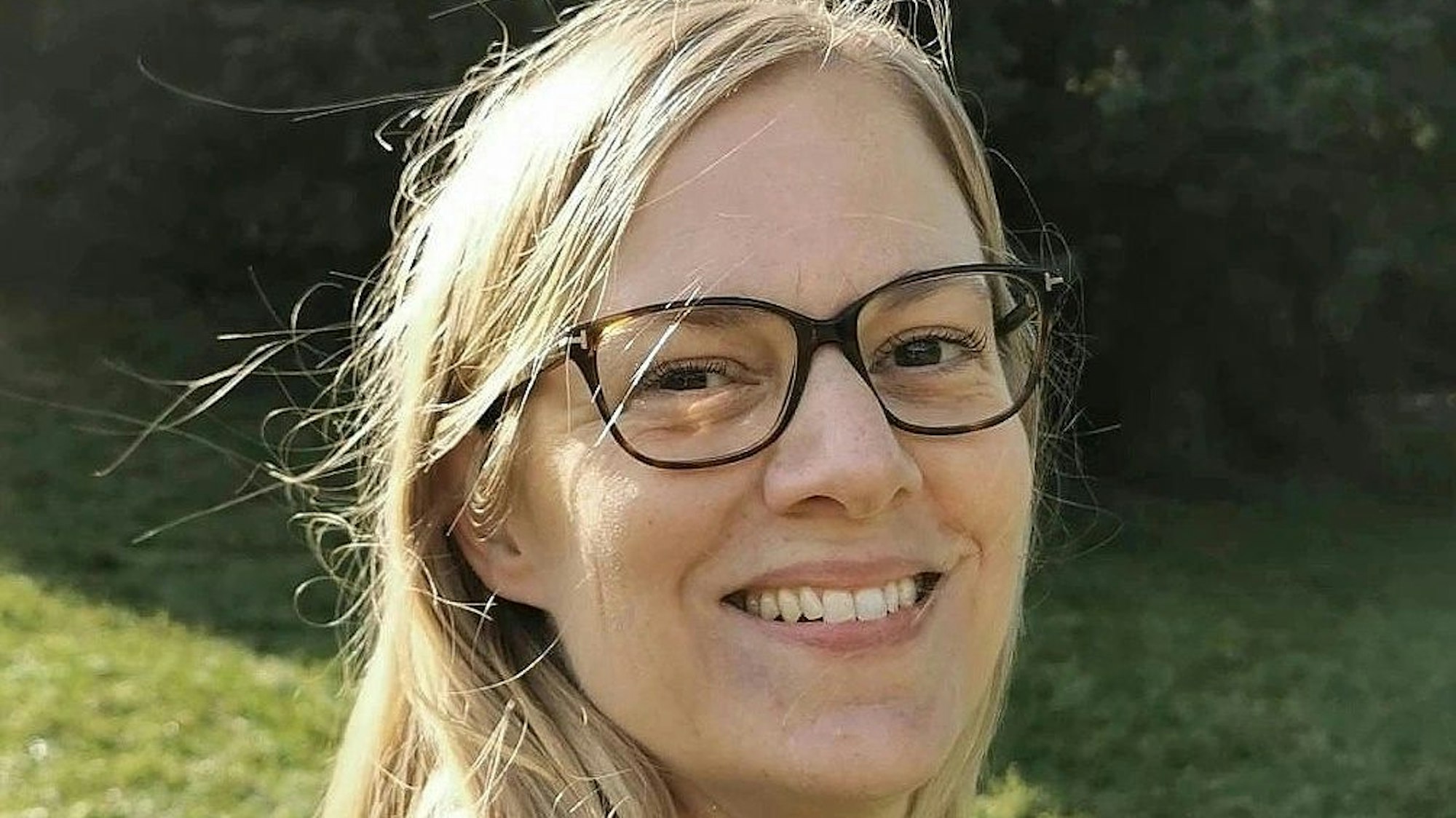 Eine blonde Frau mit blauer Bluse und schwarzer Brille.