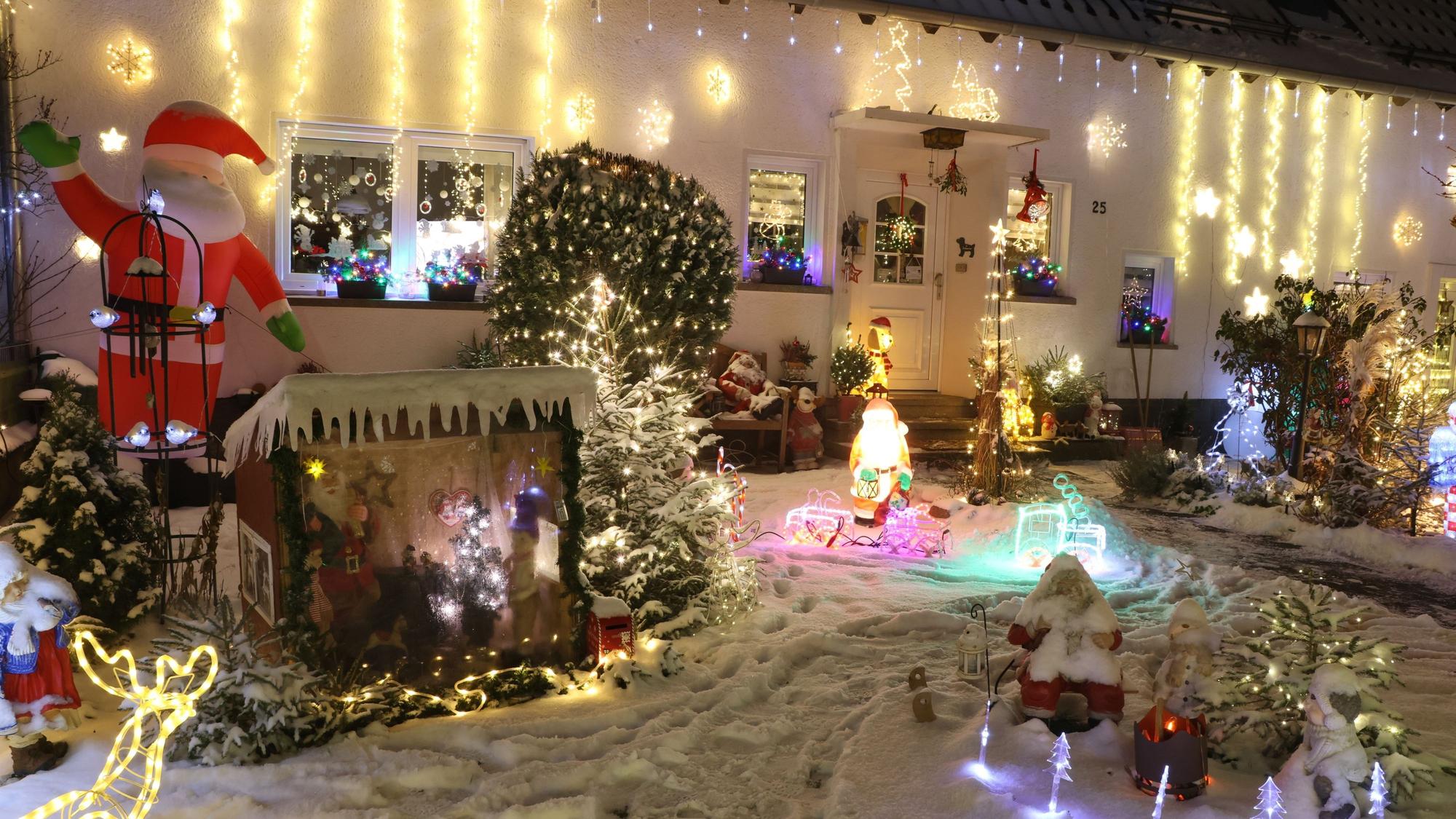 Vor einem Haus leuchten zahlreiche weihnachtliche Figuren und Lichterketten in bunten Farben. Ein aufblasbarer Nikolaus winkt.