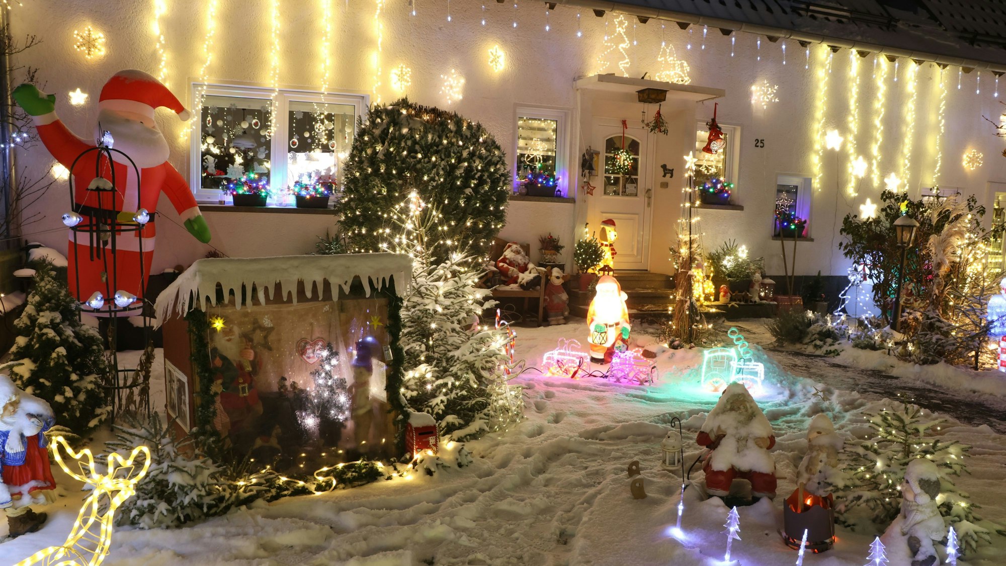 Vor einem Haus leuchten zahlreiche weihnachtliche Figuren und Lichterketten in bunten Farben. Ein aufblasbarer Nikolaus winkt.