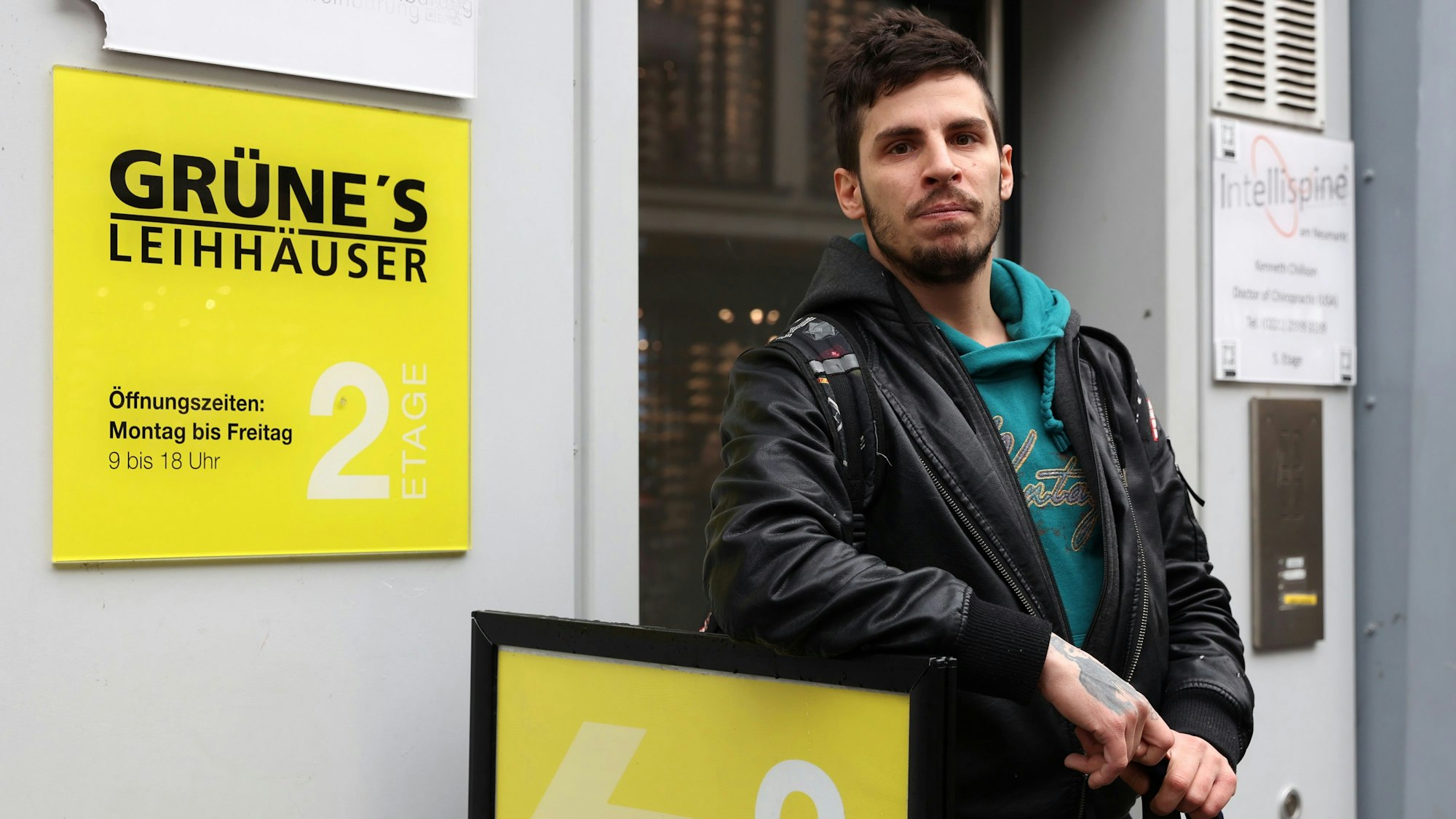 Ein junger Mann mit Bart steht neben dem Geschäftsschild von „Grüne's Leihhaus“ in der Kölner Schildergasse.