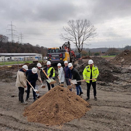 Mit Spaten in der Hand stehen vor einem Sandhaufen Roman Stach (Projektleiter Goldbeck), FB-Leiter Ingolf Bergerhoff, Stephan Bergmann (Amt für Gebäudewirtschaft), FB-Leiterin Mirjam Bosse, Bürgermeister Frank Steffes und Kämmerer Thomas Knabbe