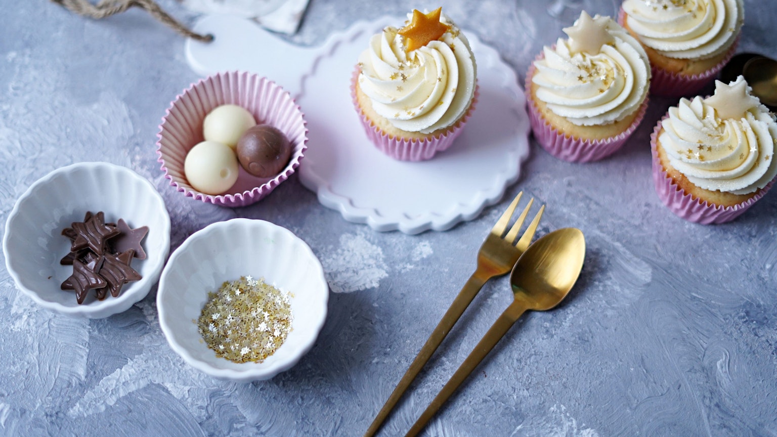 Die Cupcakes stehen verziert in pinken Förmchen auf einem weihnachtlich gedeckten Tisch.