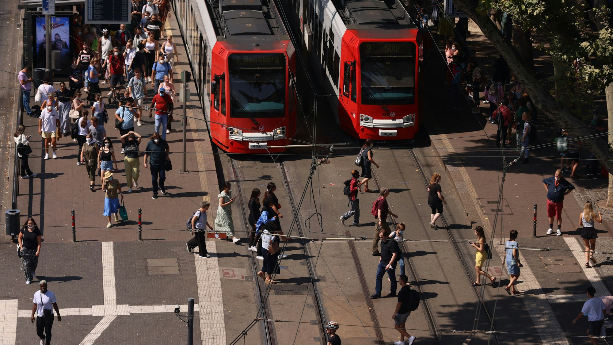 Zwei Stadtbahnen stehen am Neumarkt, während Menschen über den Gleisübergang laufen.