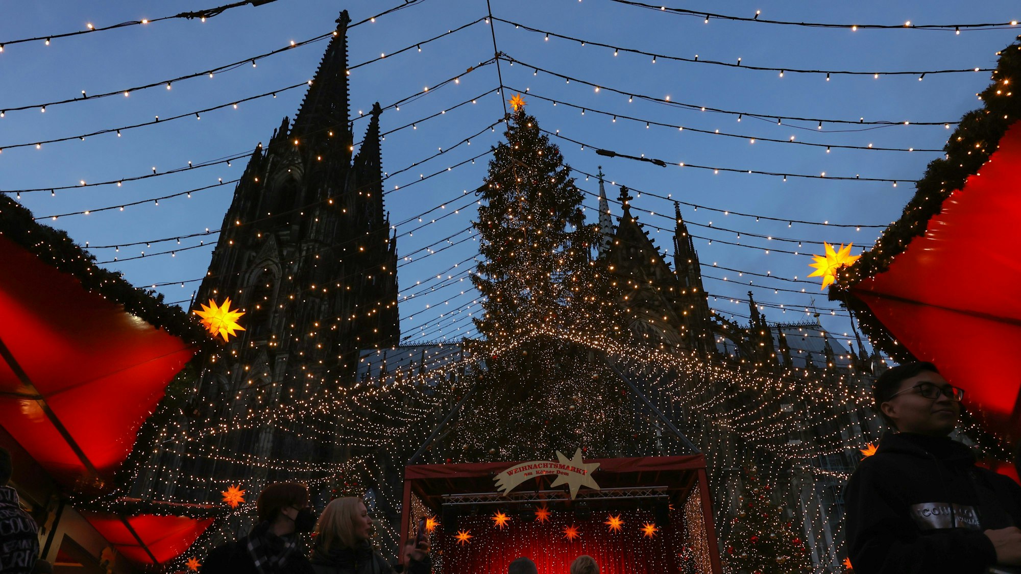 Die Spitzen des Kölner Dom erheben sich hinter dem Weihnachtsmarkt auf dem Roncalliplatz.