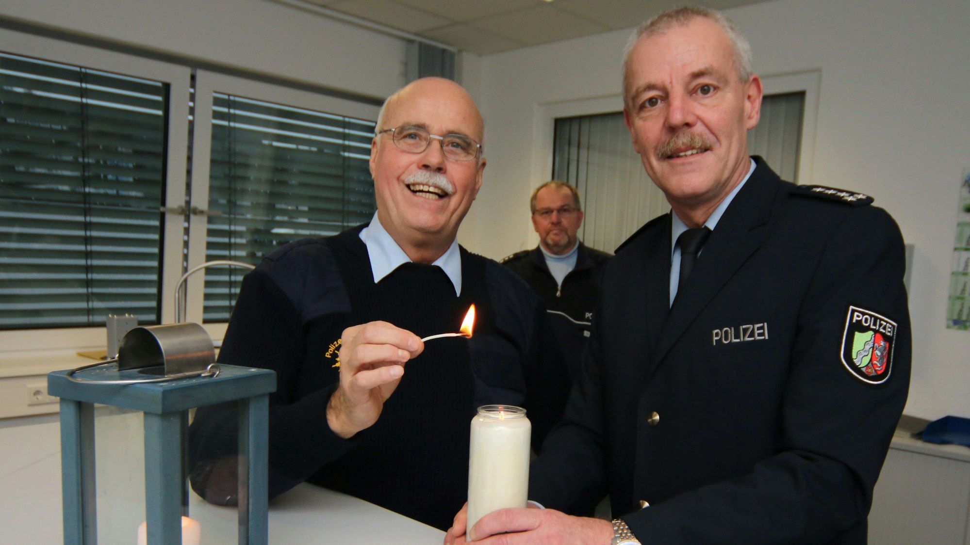 Ein Polizeiseelsorger zündet eine Kerze an. Im Vordergrund steht eine Laterne, daneben ein Schild mit der Aufschrift „Licht von Bethlehem“.