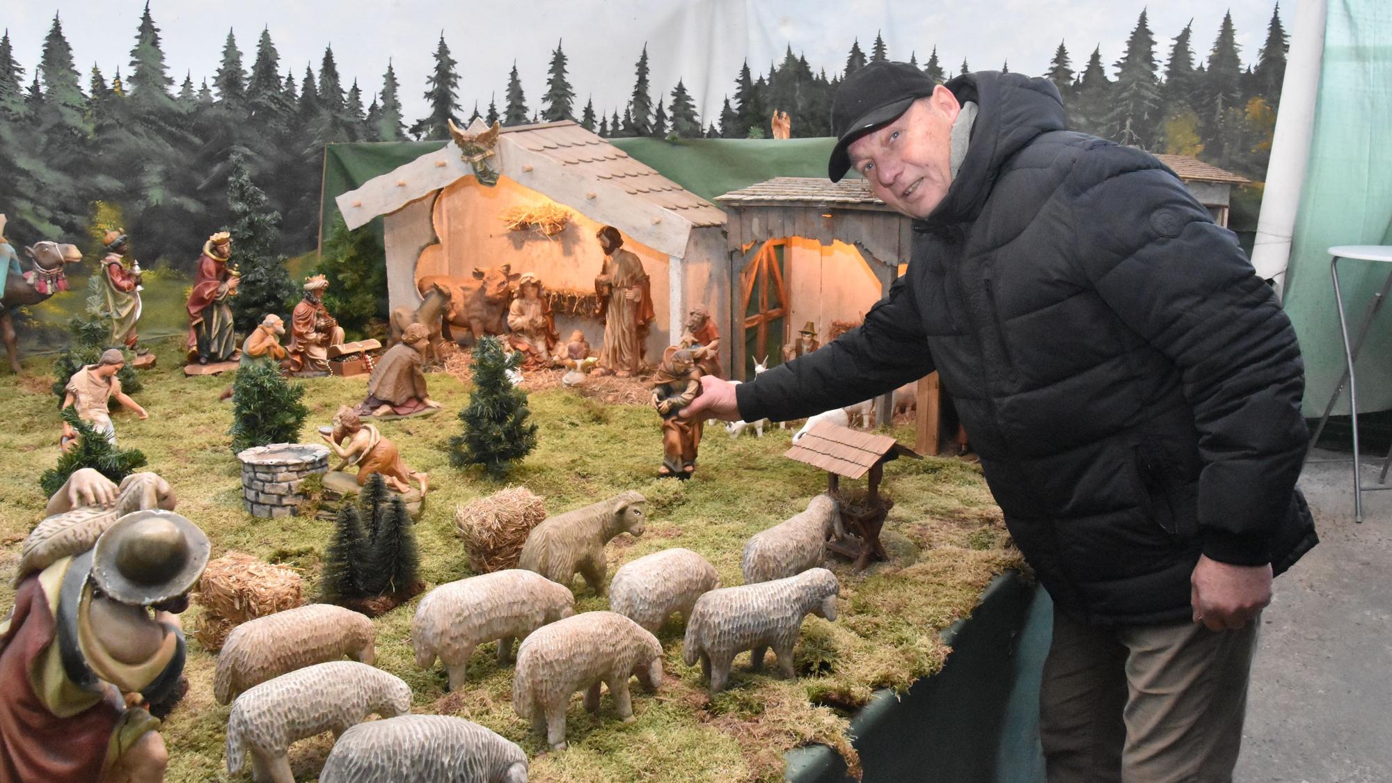 Ein Mann stellt eine Figur in eine Krippenlandschaft.